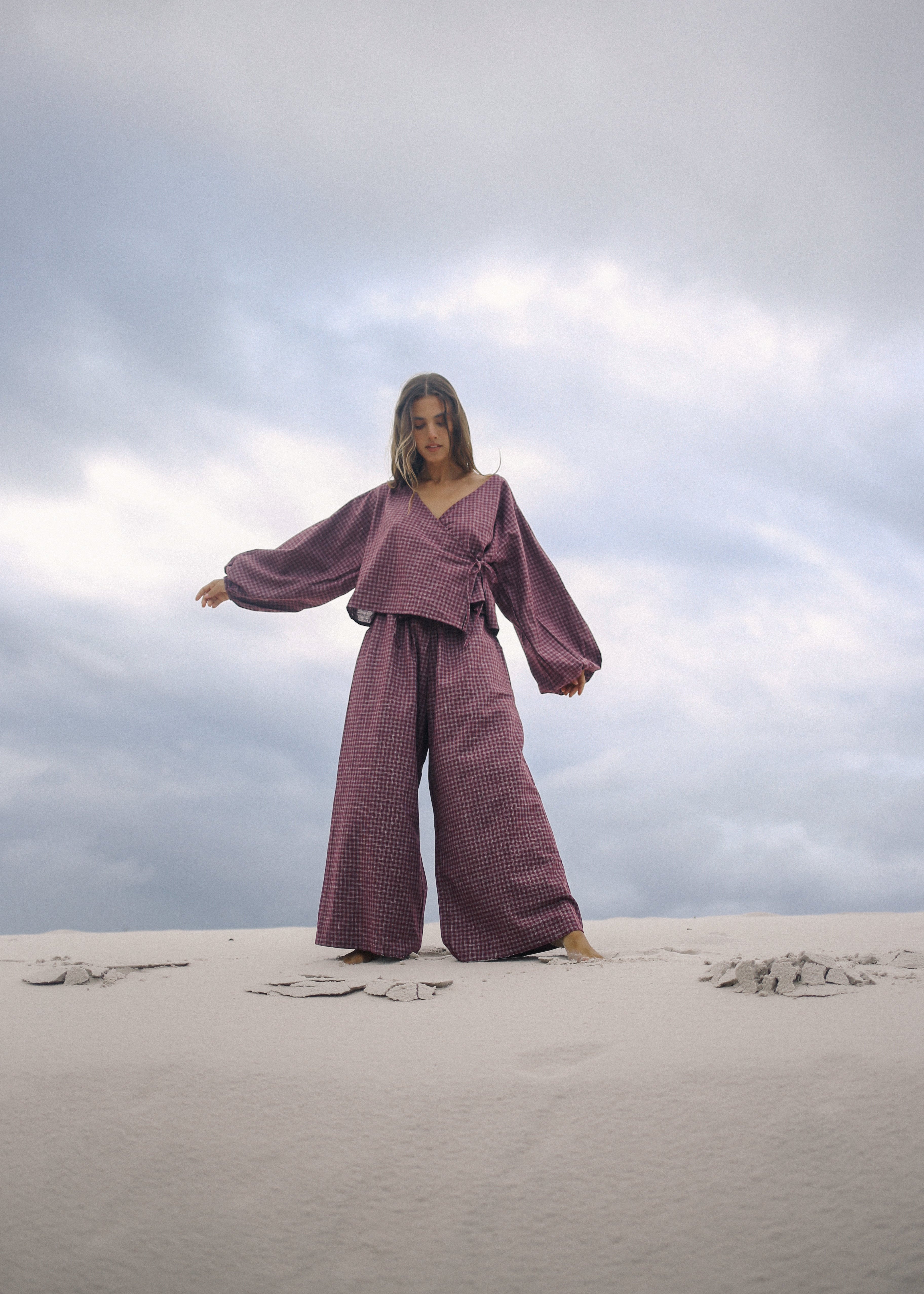 Person wearing a purple outfit standing on sand with a cloudy sky.