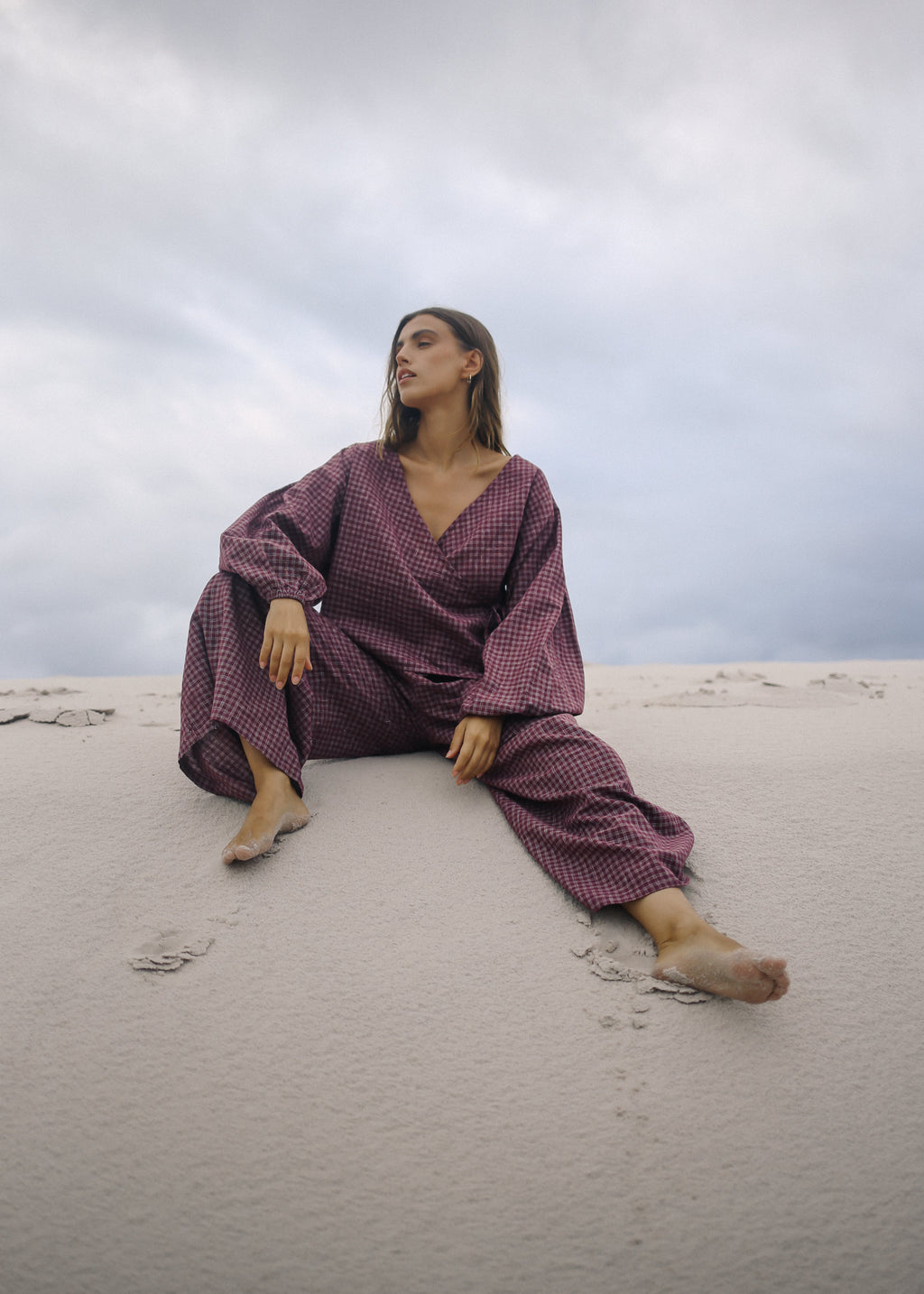 Woman in a purple outfit sitting on sand with a cloudy sky.