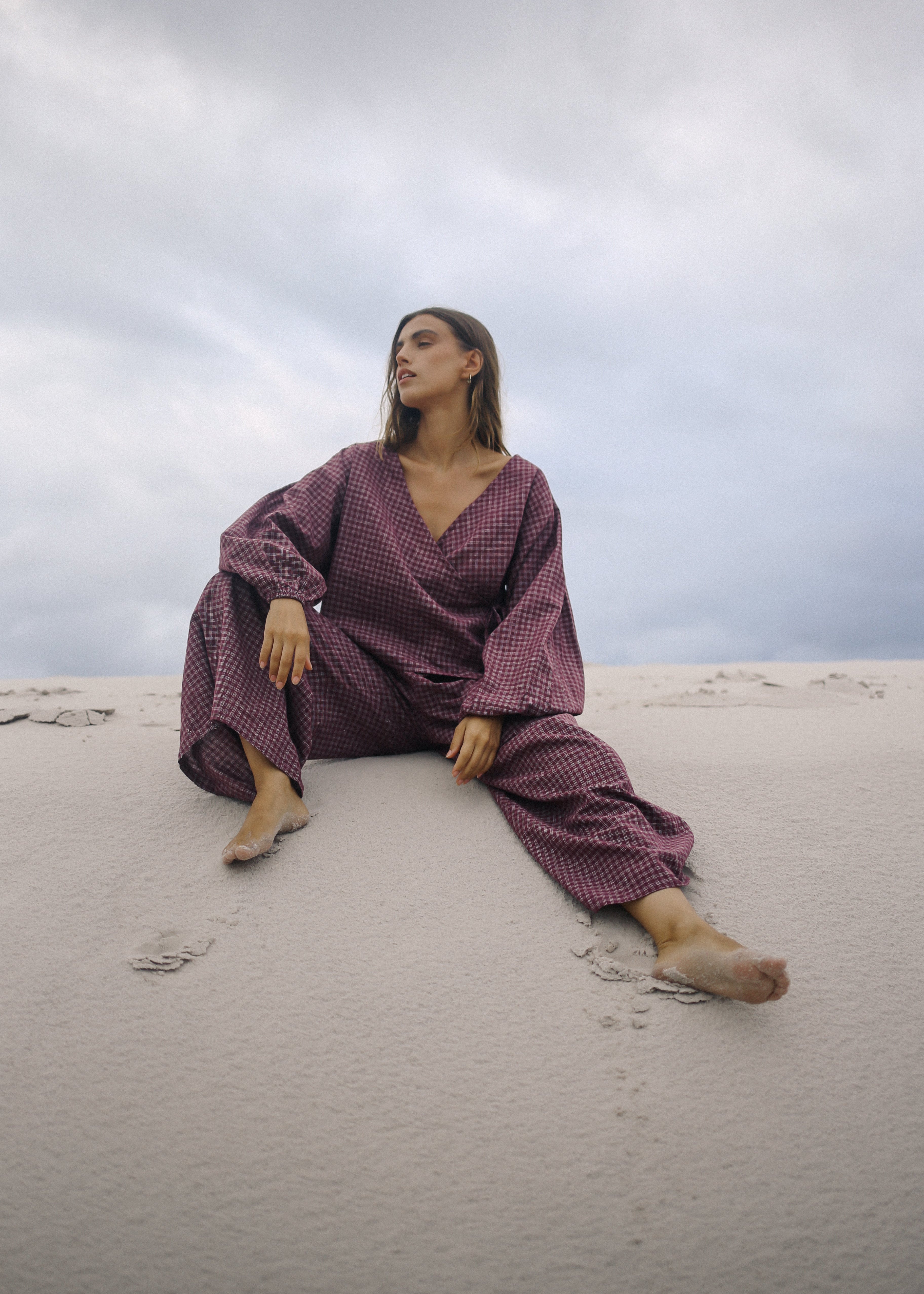 Woman in a purple outfit sitting on sand with a cloudy sky.