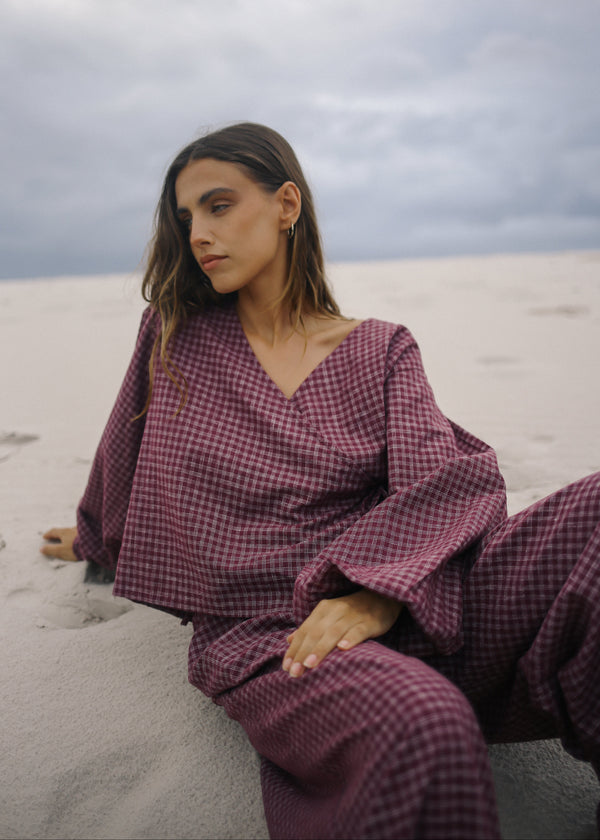 Woman in a purple checkered outfit sitting on sand with a cloudy sky.