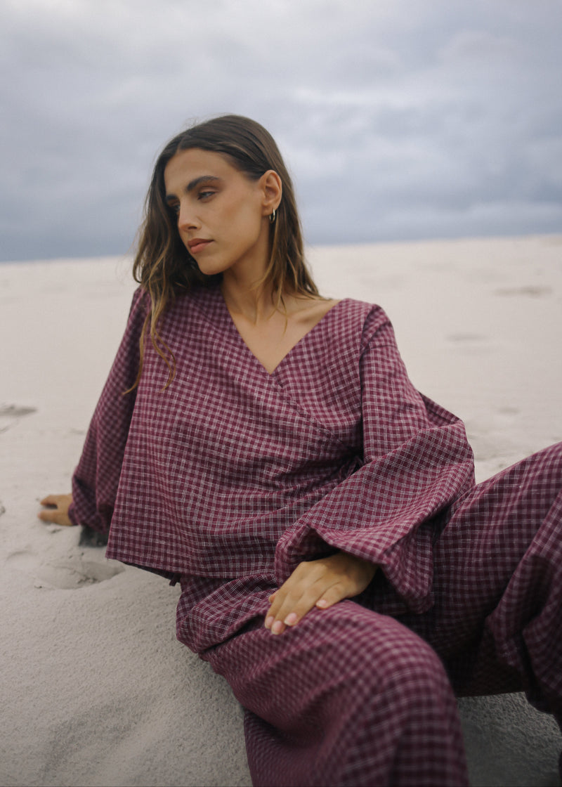 Woman in a purple checkered outfit sitting on sand with a cloudy sky.