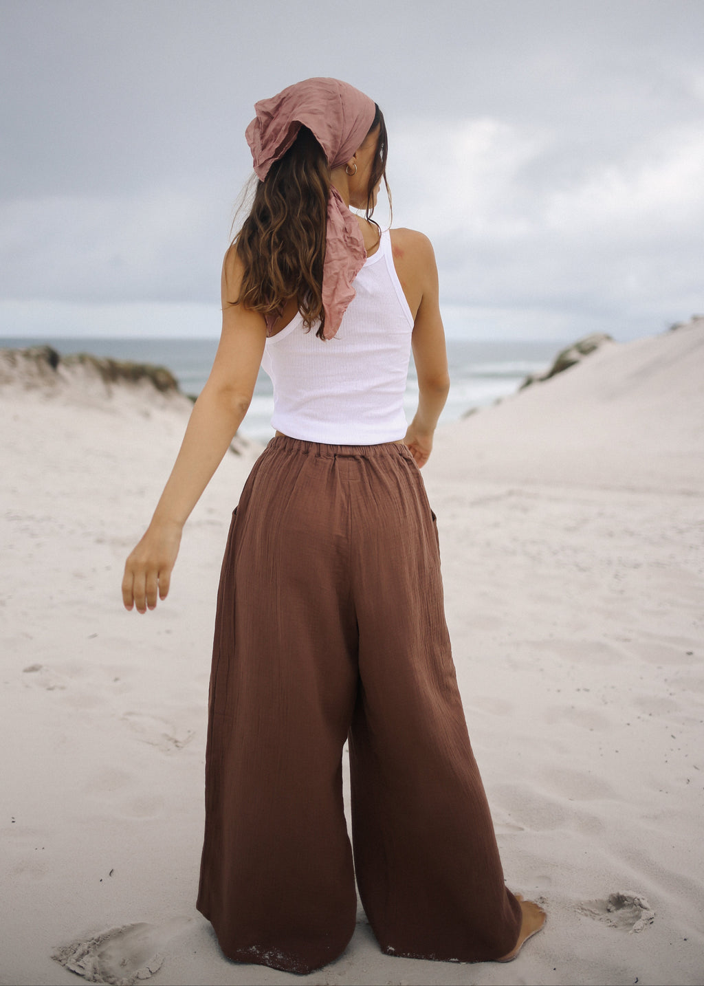 Person wearing a white top and brown wide-leg pants on a sandy beach.
