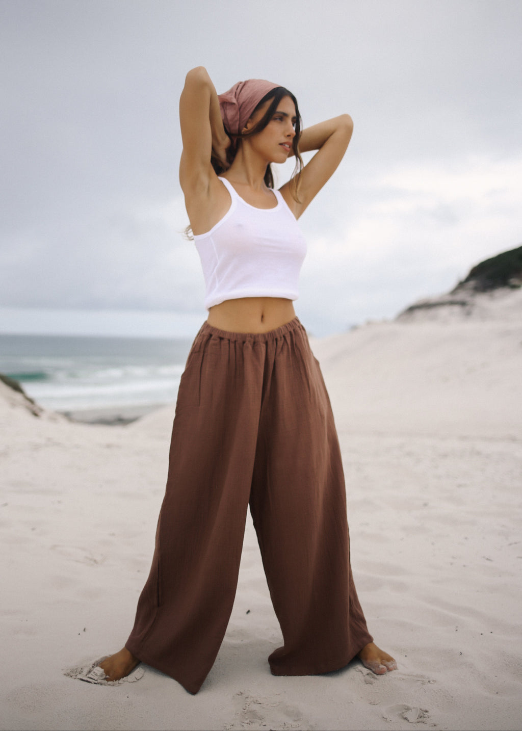 Woman in white tank top and brown wide-leg pants on a beach