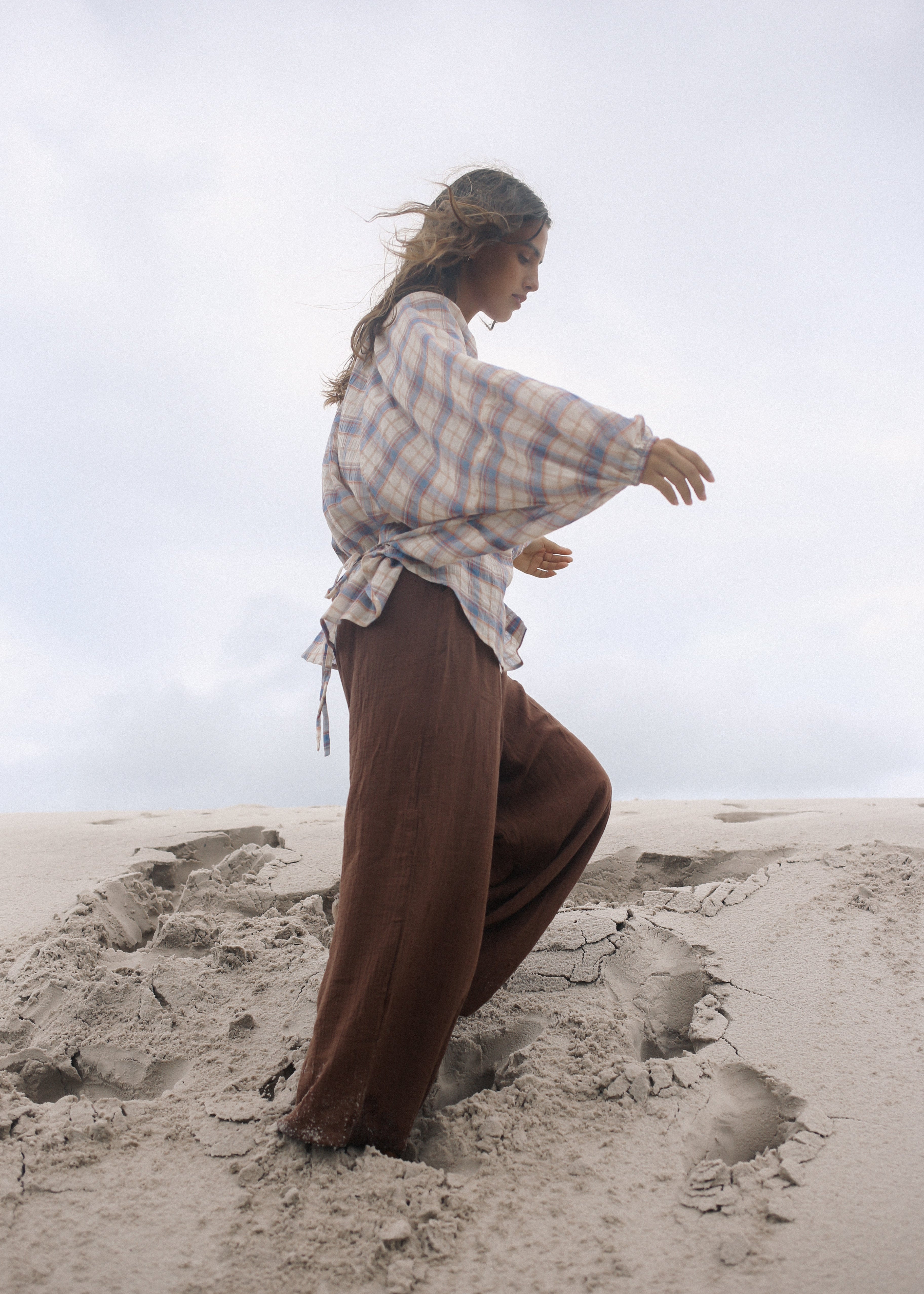 Person in historical attire standing on a sandy beach with a cloudy sky.