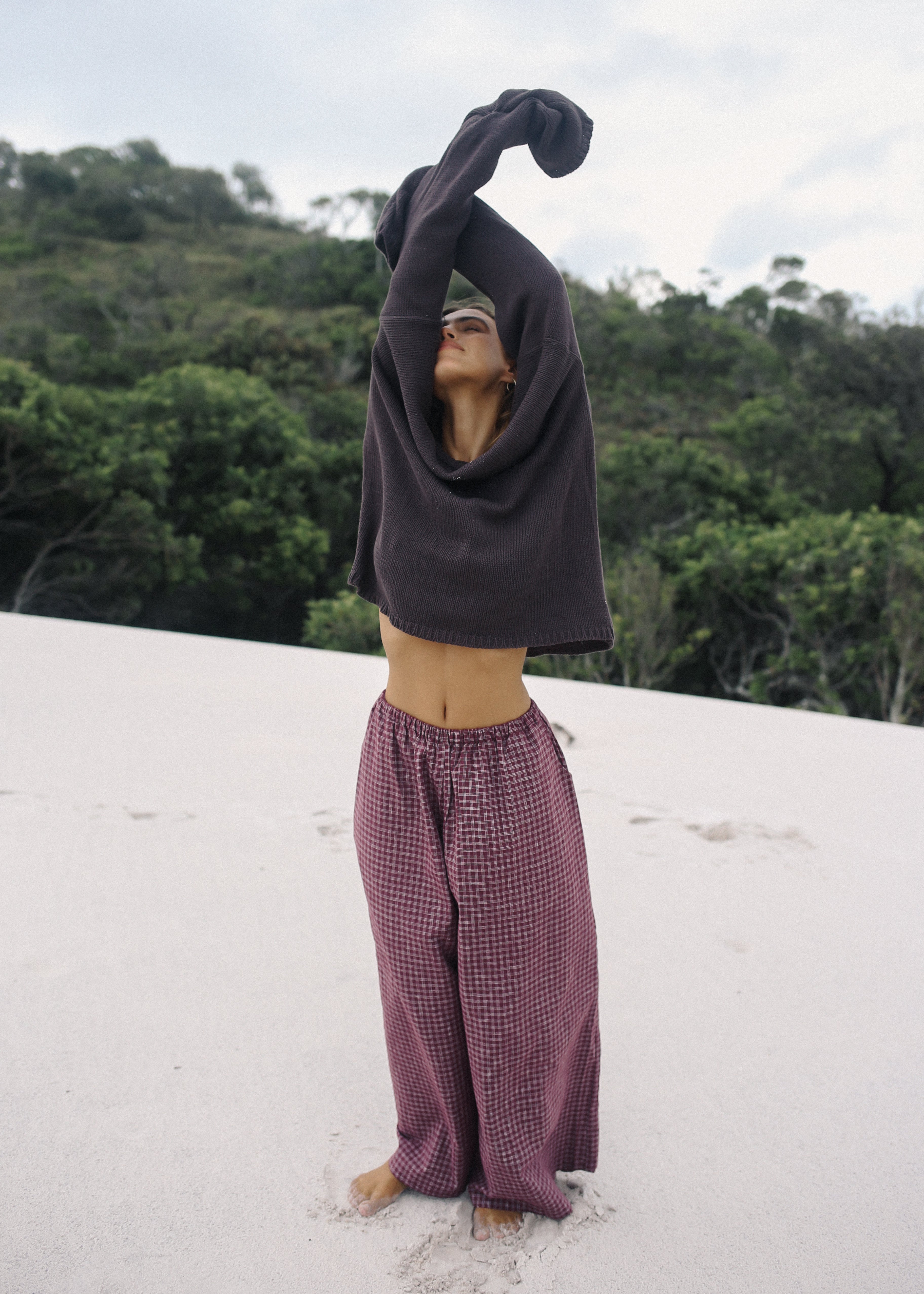 Person in a dark hoodie and checkered pants standing on a white surface with a forest background