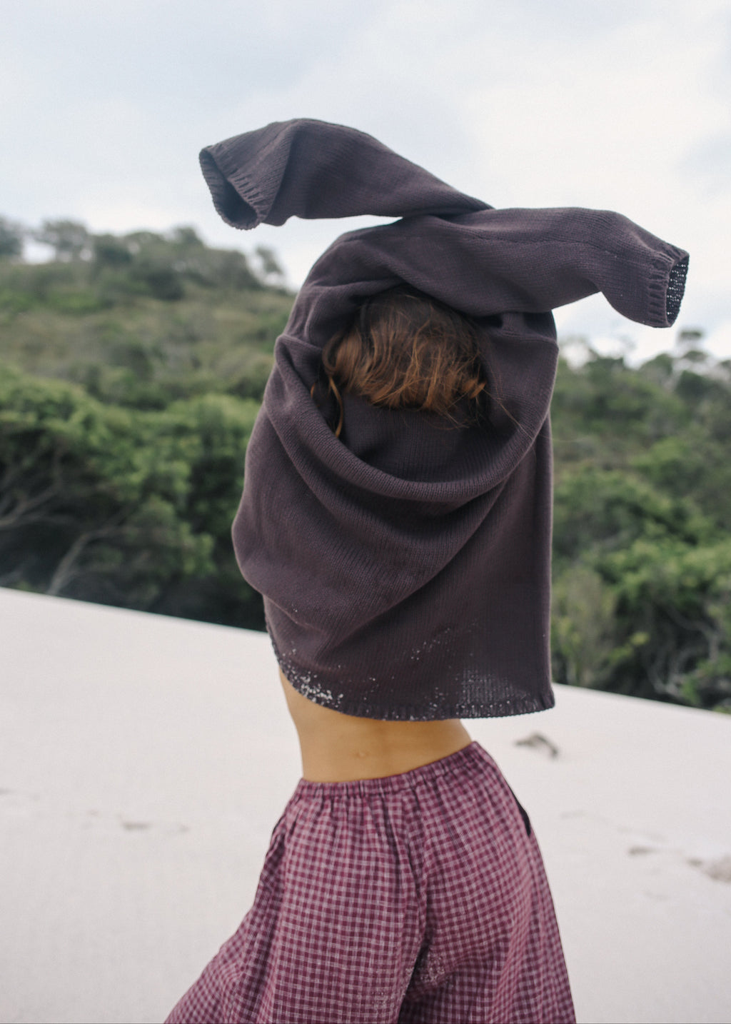 Person wearing a dark hooded garment with a blurred natural background