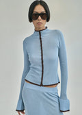 Woman wearing a light blue ribbed outfit with a dark zipper on a gray background