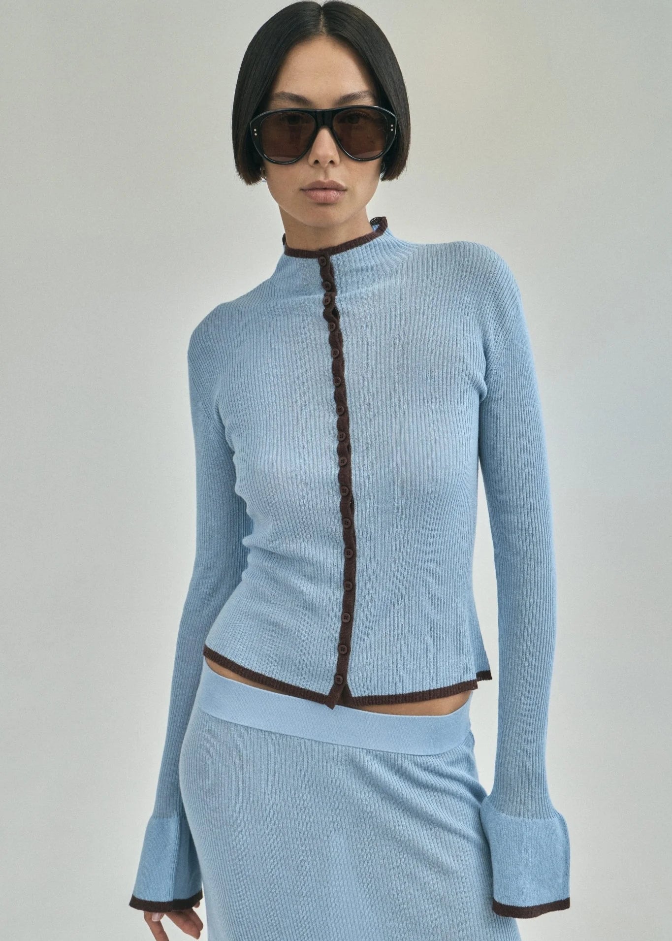 Woman wearing a light blue ribbed outfit with a dark zipper on a gray background
