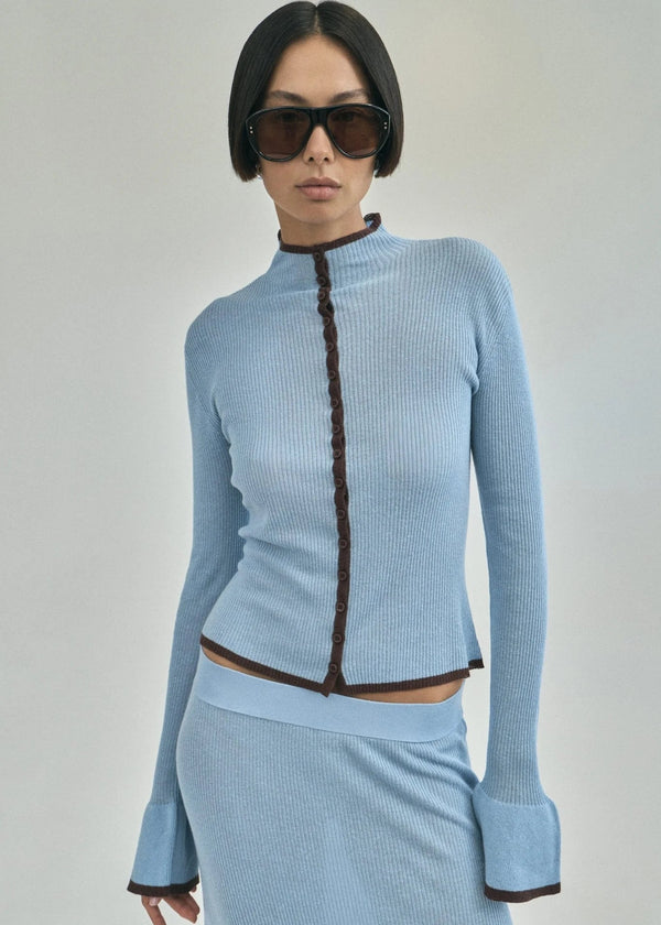 Woman wearing a light blue ribbed outfit with a dark zipper on a gray background