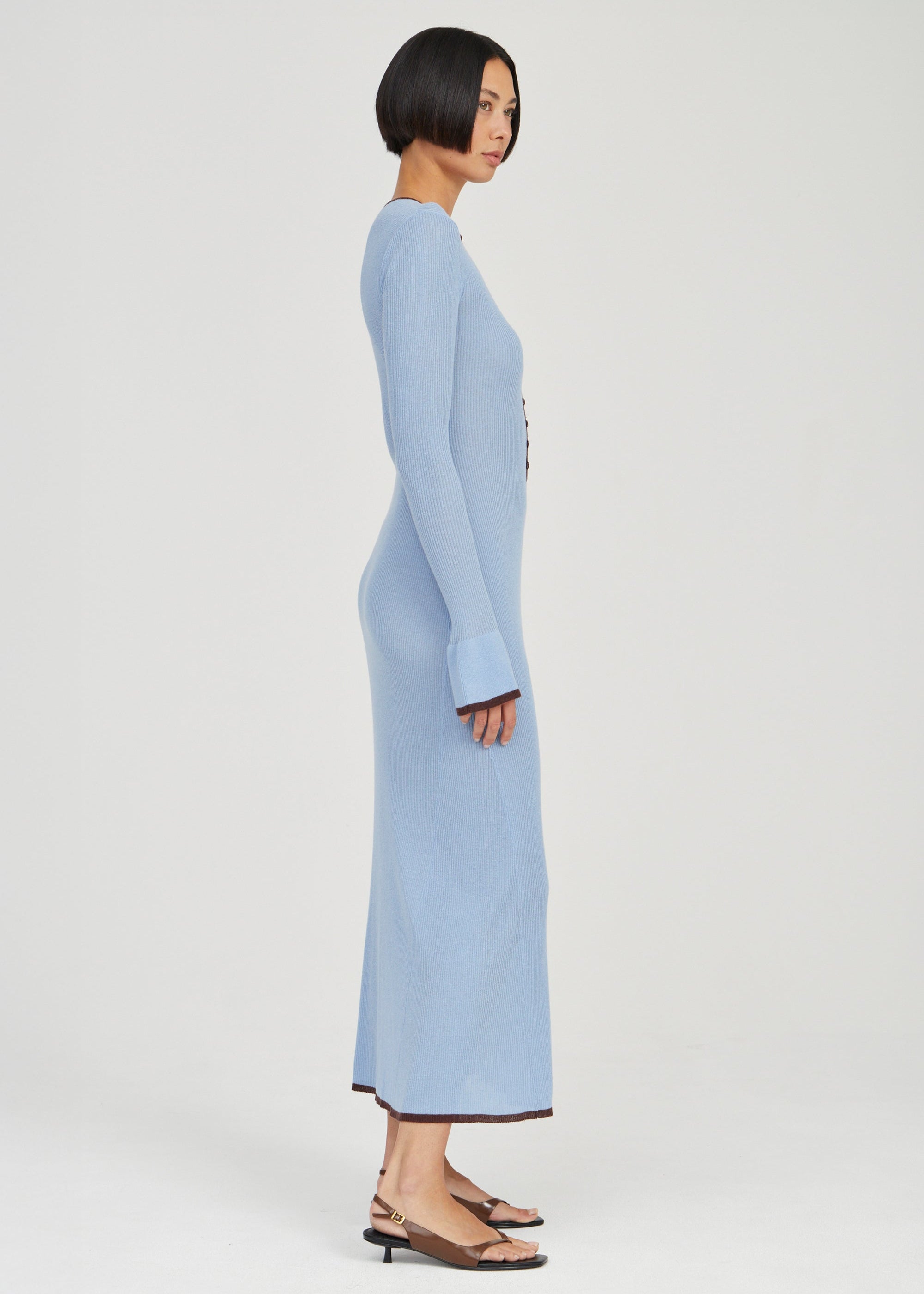 A woman modeling a light blue long-sleeve maxi dress, shown from a side profile against a plain light gray studio background.