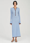 A model wearing a light blue long-sleeve maxi dress with a dark brown trim detail down the front neckline and along the hem, paired with black sandals, against a light gray studio background.