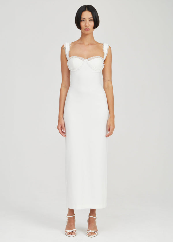 A woman modeling a white sleeveless midi dress with a structured sweetheart neckline, ruffled shoulder straps, and a fitted silhouette, photographed against a light gray studio background.