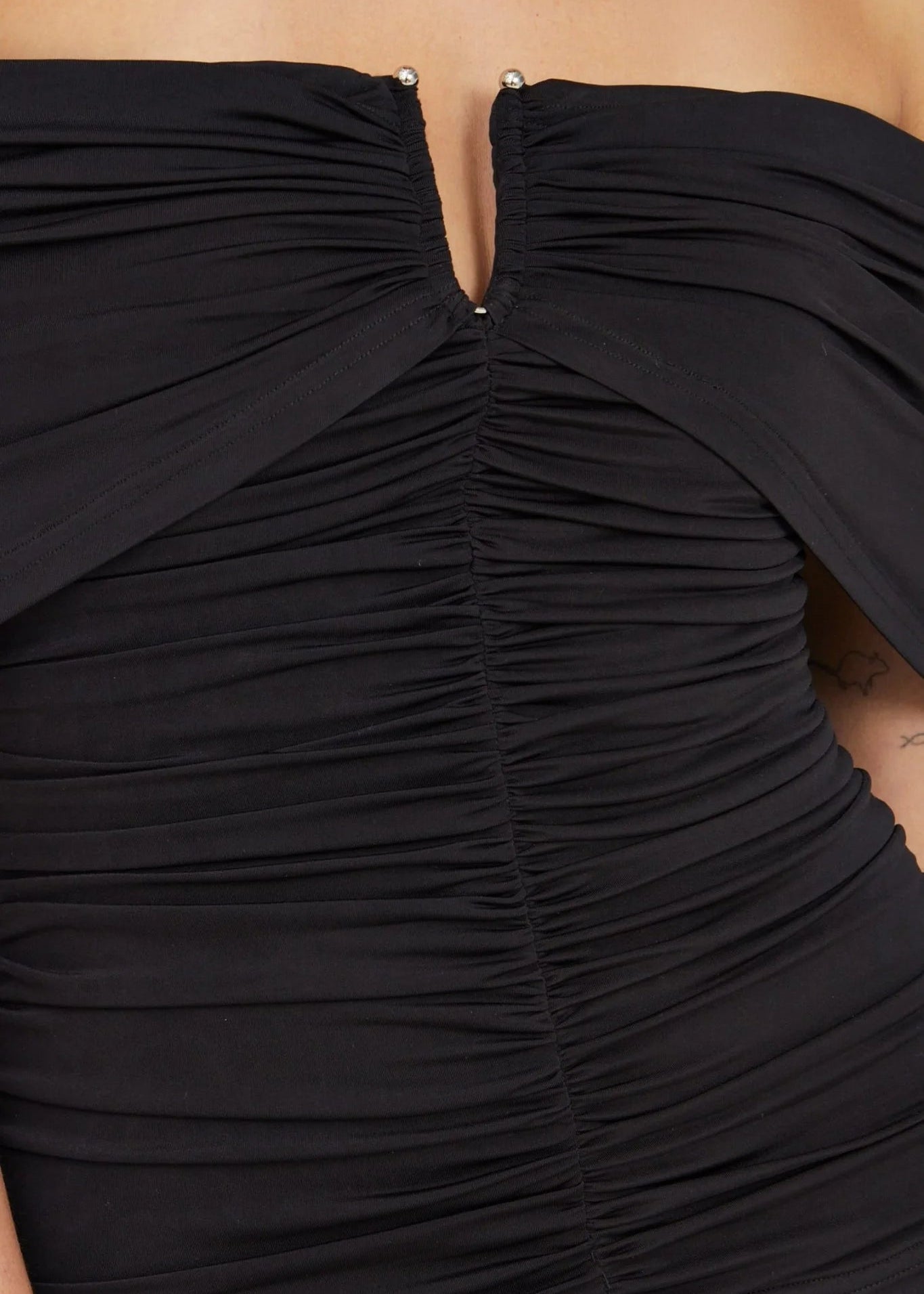 Close-up of a black off-the-shoulder ruched top with a split neckline and small silver bead accents, shown on a model.