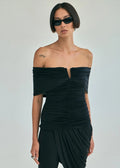 A model wearing a black off-the-shoulder ruched top and matching draped pants against a light gray studio background.