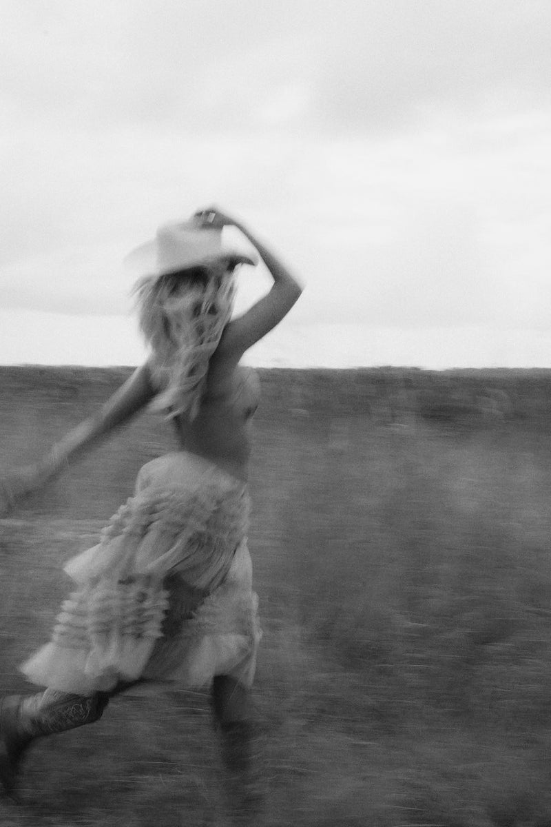 Person in a dress and hat running in an open field