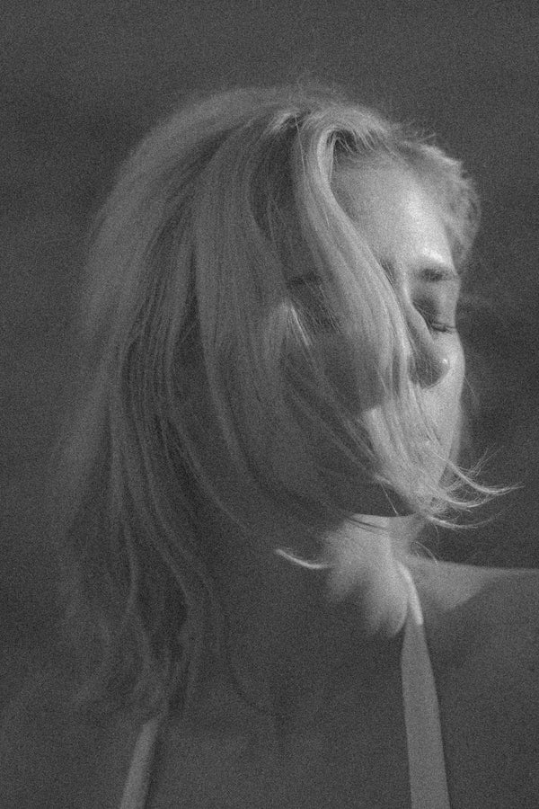 Black and white close-up of a person with hair blowing in the wind against a dark background