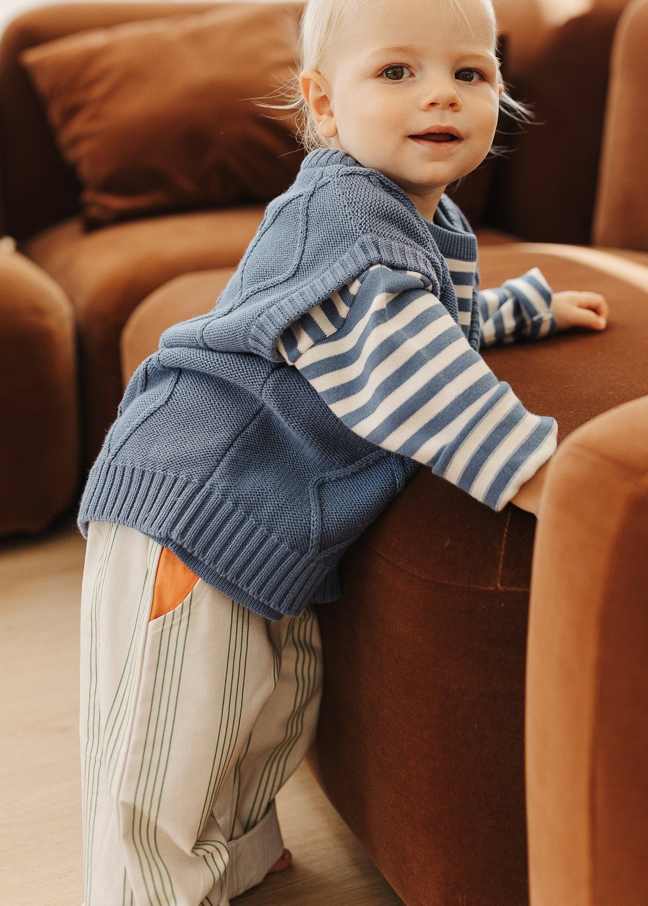 Child in a blue sweater and striped shirt standing on a brown couch