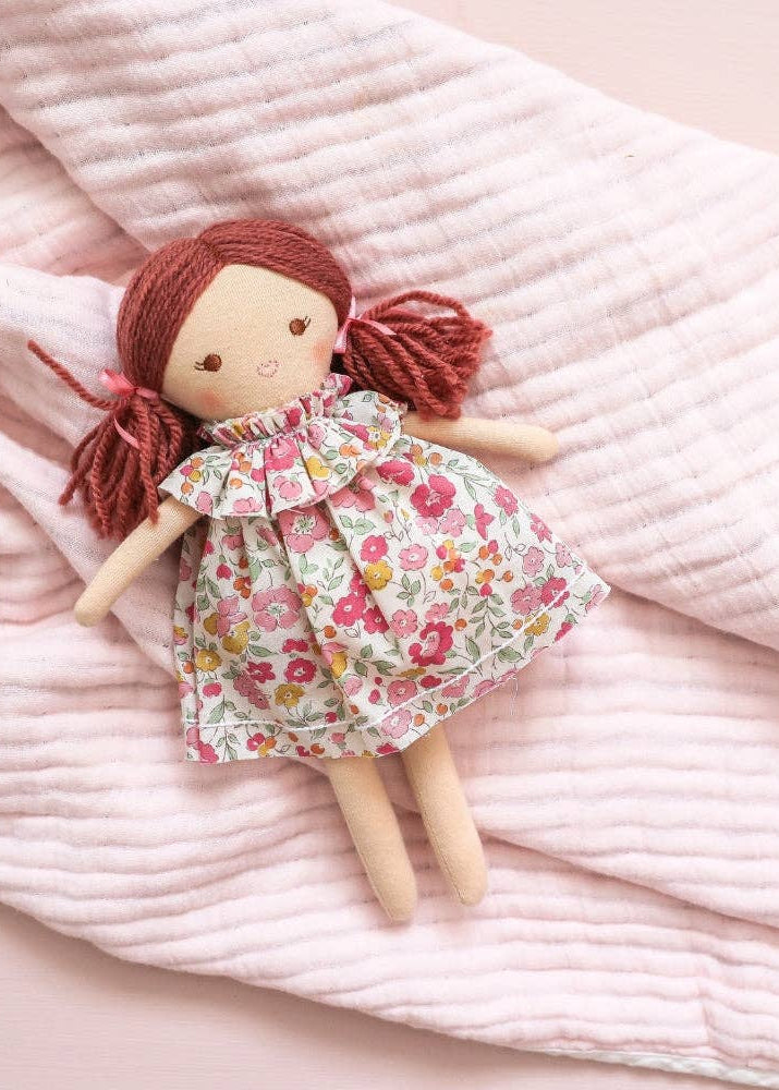 Handmade doll with red hair and a floral dress on a pink textured fabric background