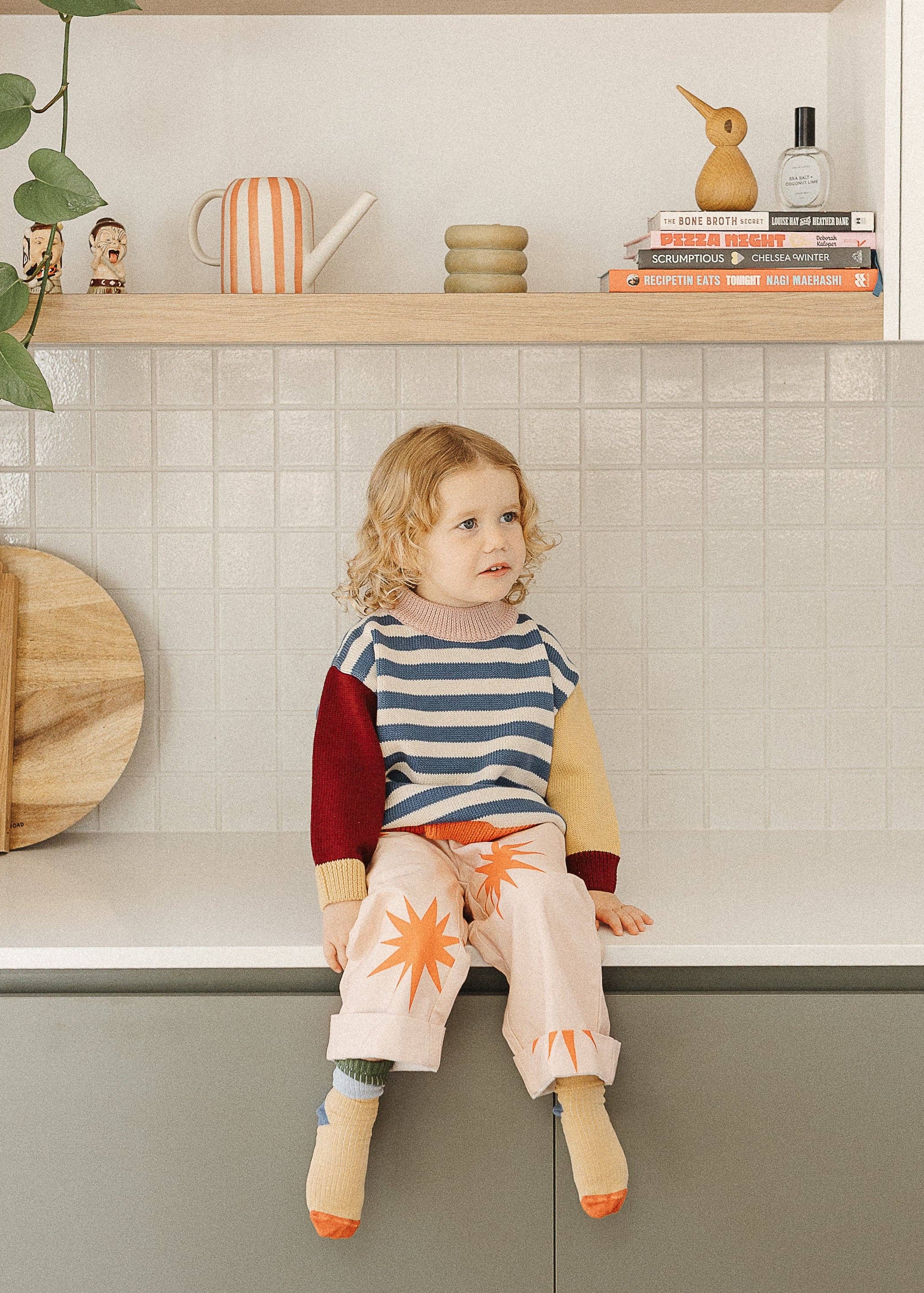 Child sitting on a kitchen counter with a shelf in the background