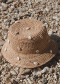 Woven straw hat with shell embellishments on a gravel surface