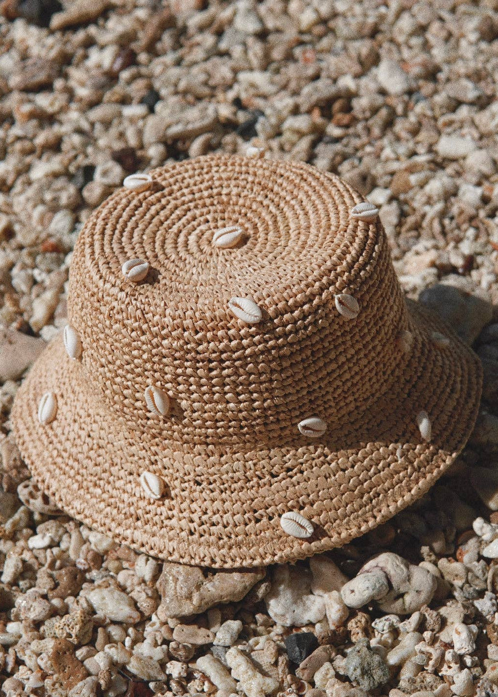 Woven straw hat with shell embellishments on a gravel surface