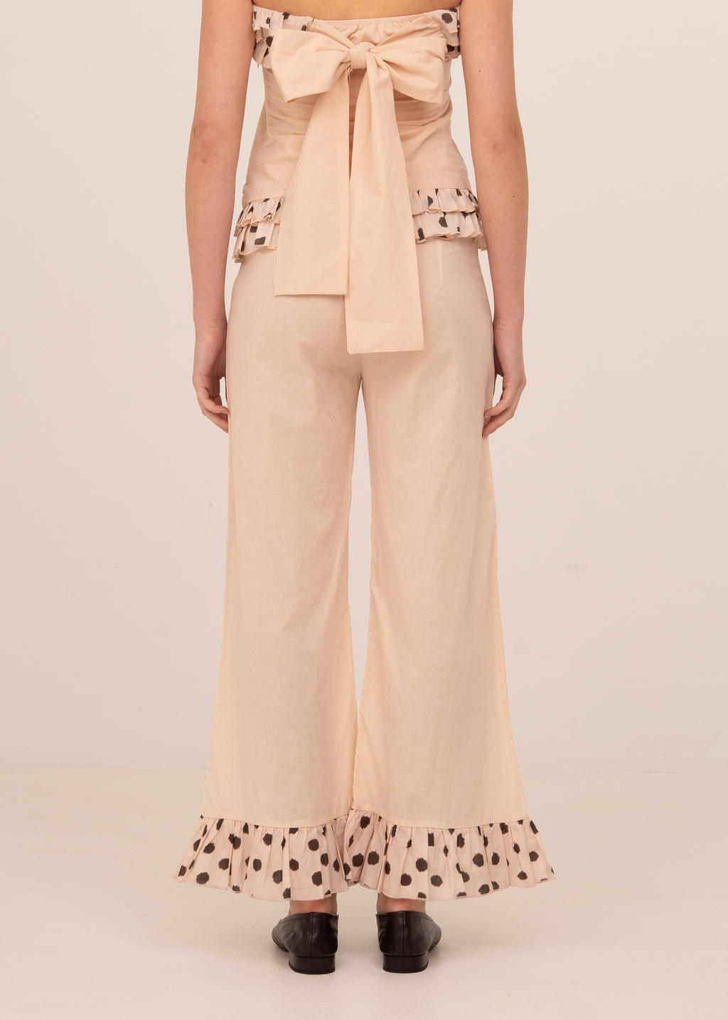 Woman wearing a beige top and wide-leg pants with polka dot trim on a beige background