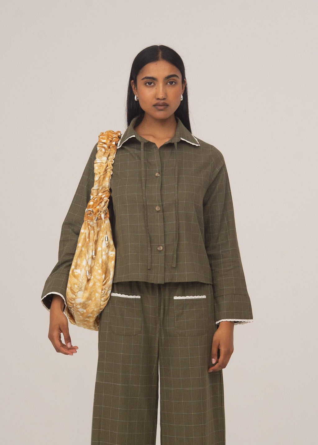 Woman wearing a green checkered outfit holding a beige bag against a plain background