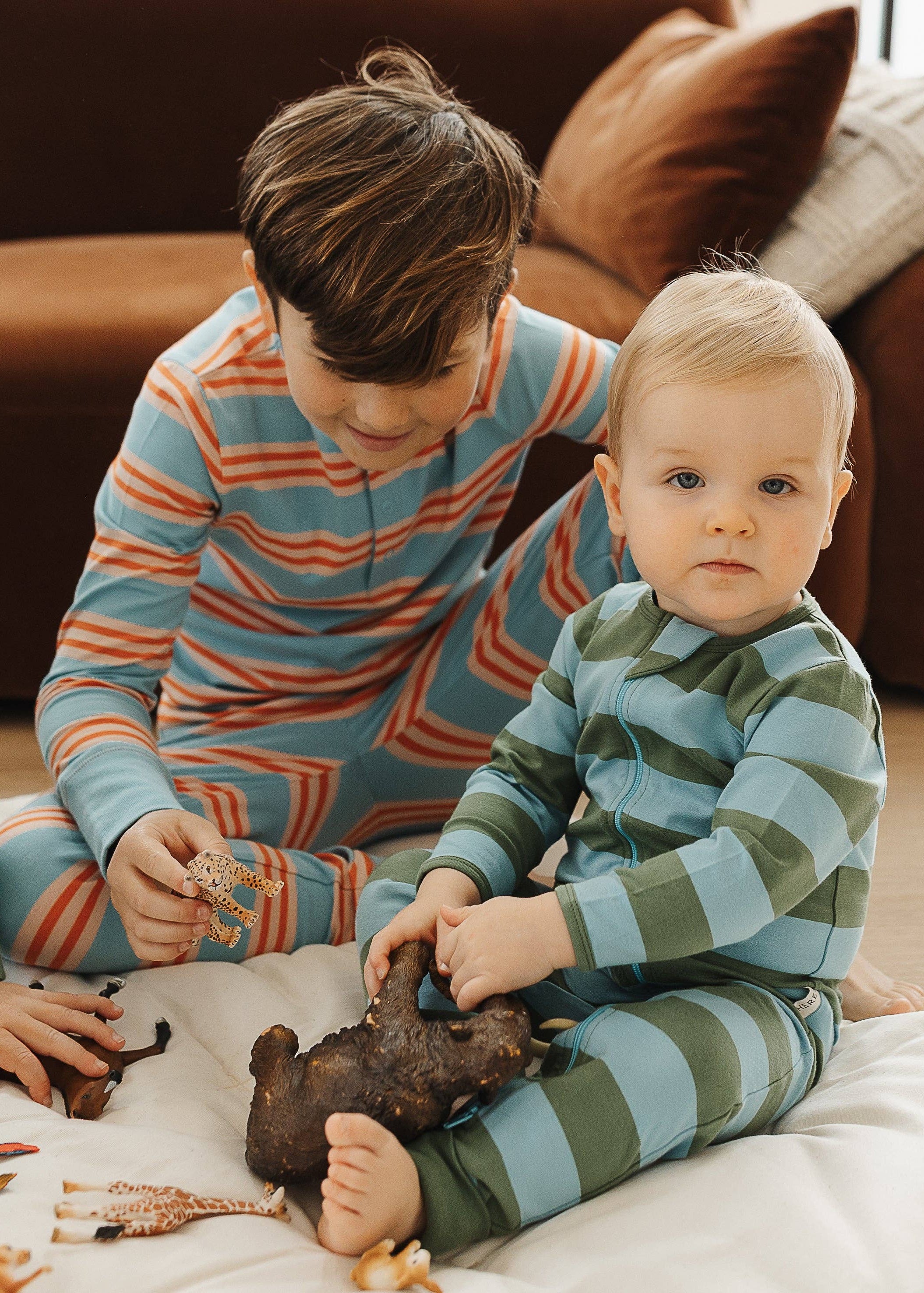 Three children in striped pajamas playing with toys on a bed.
