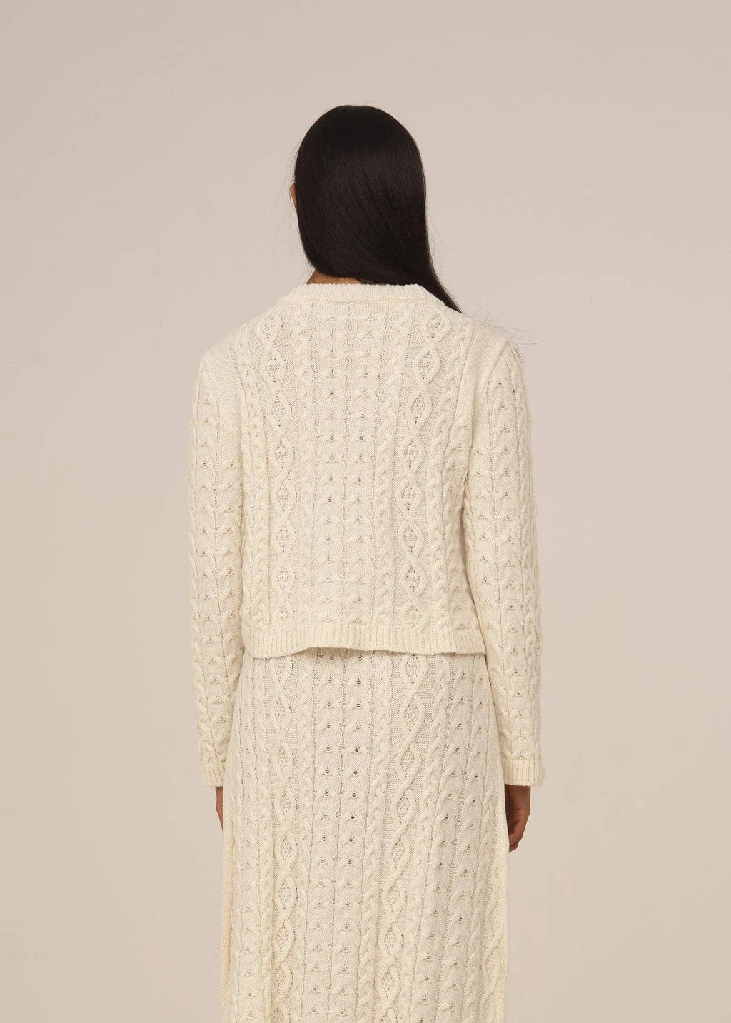 Person wearing a cream cable knit outfit against a beige background