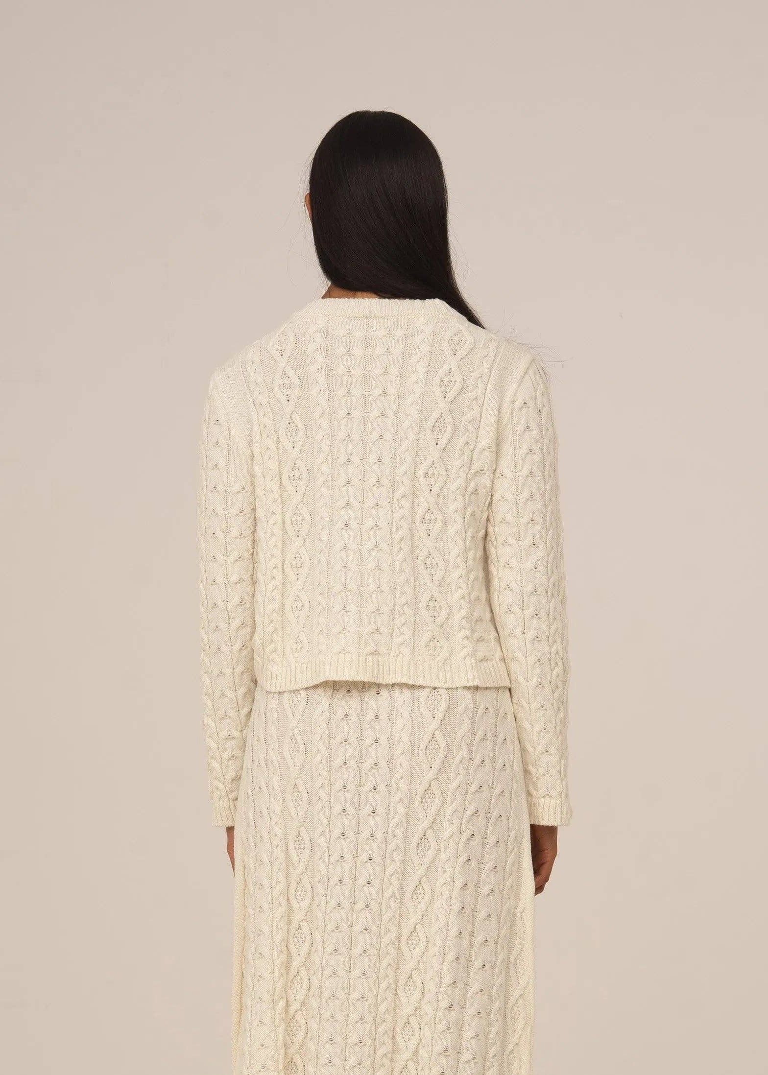 Person wearing a cream cable knit outfit against a beige background