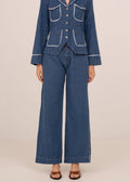Person wearing a blue denim outfit with a jacket and wide-leg pants on a beige background