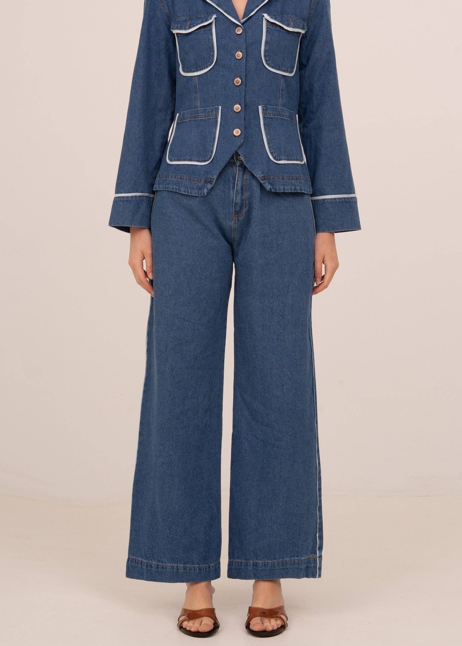 Person wearing a blue denim outfit with a jacket and wide-leg pants on a beige background