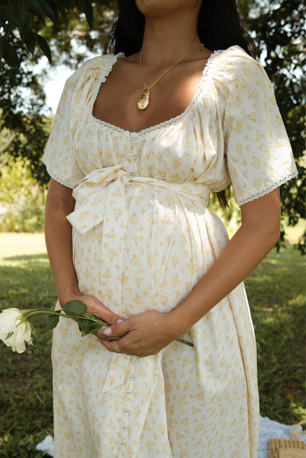Pregnant woman in a floral dress holding a flower in a natural setting