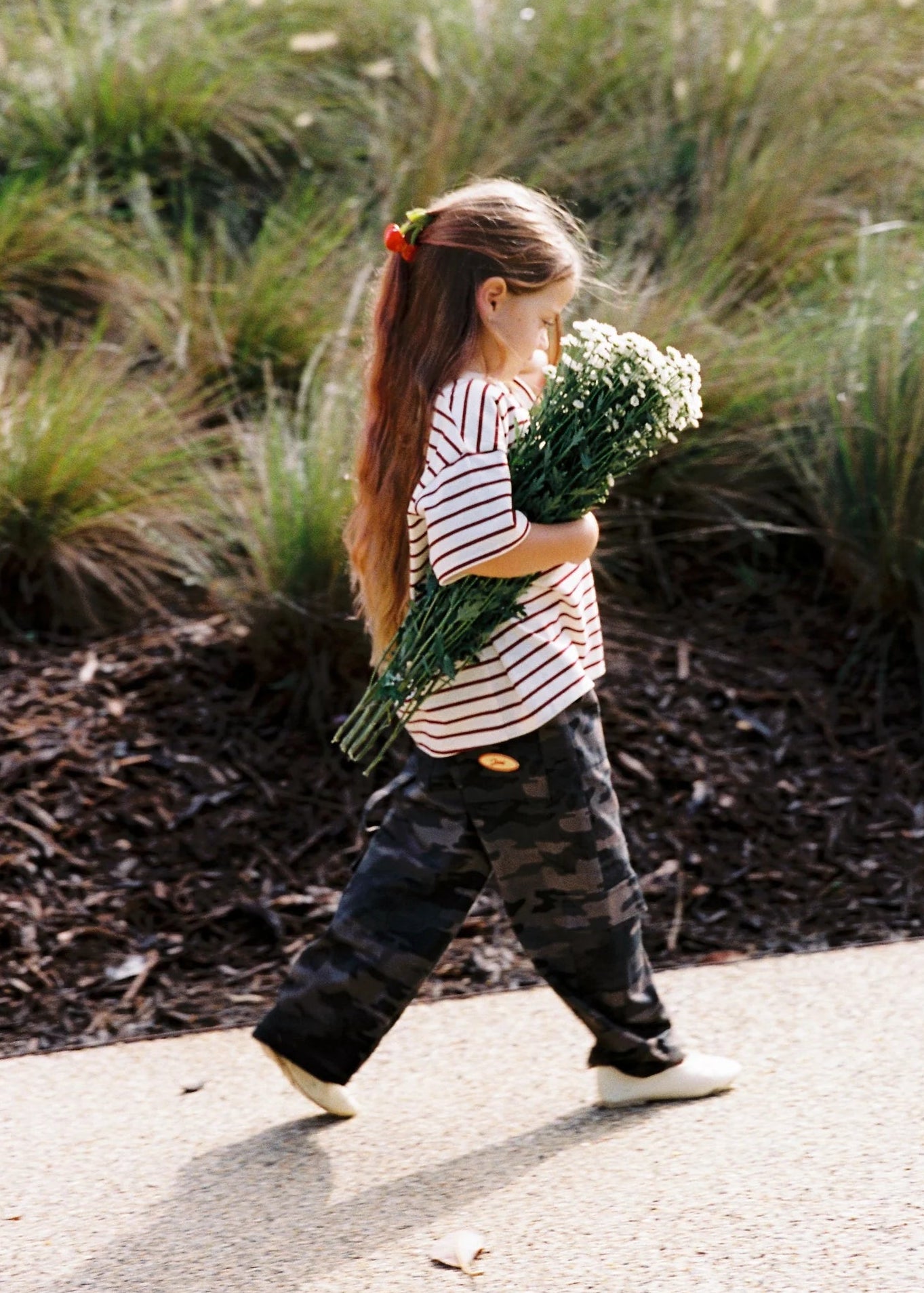 Child walking outdoors holding a bouquet of flowers