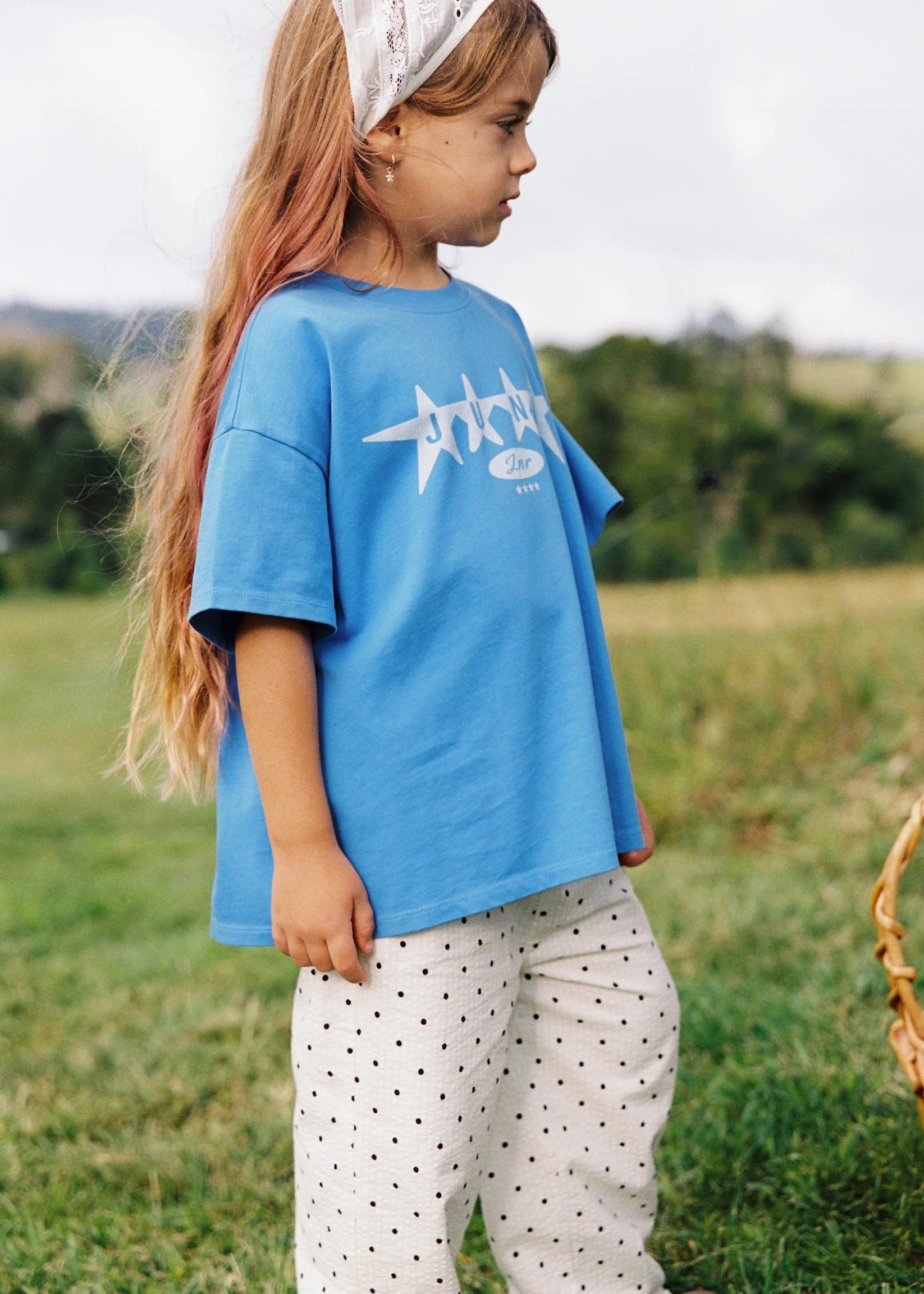 Child wearing a blue t-shirt with a logo, standing in a grassy field.