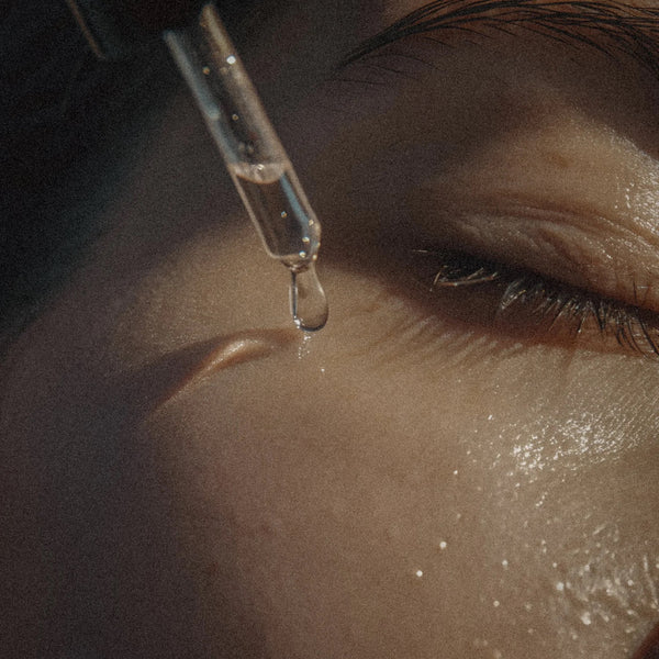 Close-up of a dropper with a drop of liquid being applied to skin near an eye.