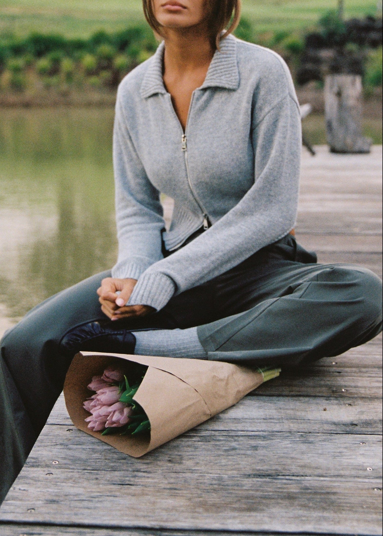 Person sitting on a wooden dock holding a bouquet wrapped in brown paper